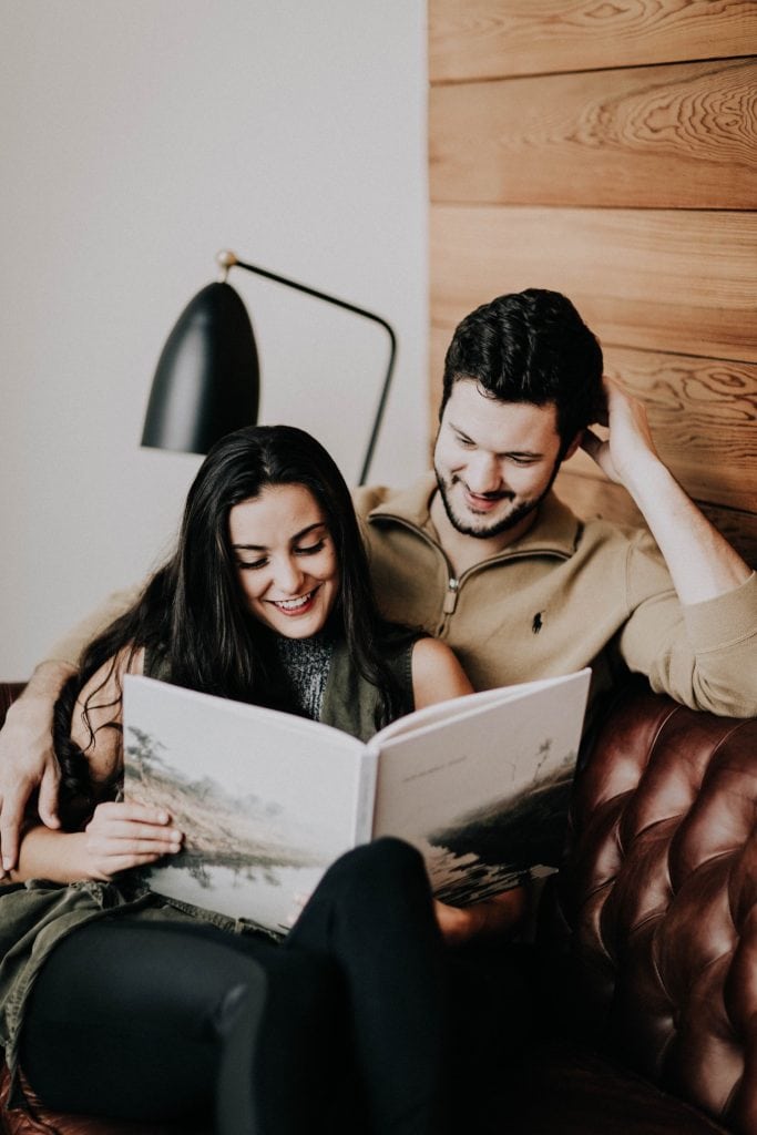 couple sitting on the couch and reading to each other during their at-home engagement photos