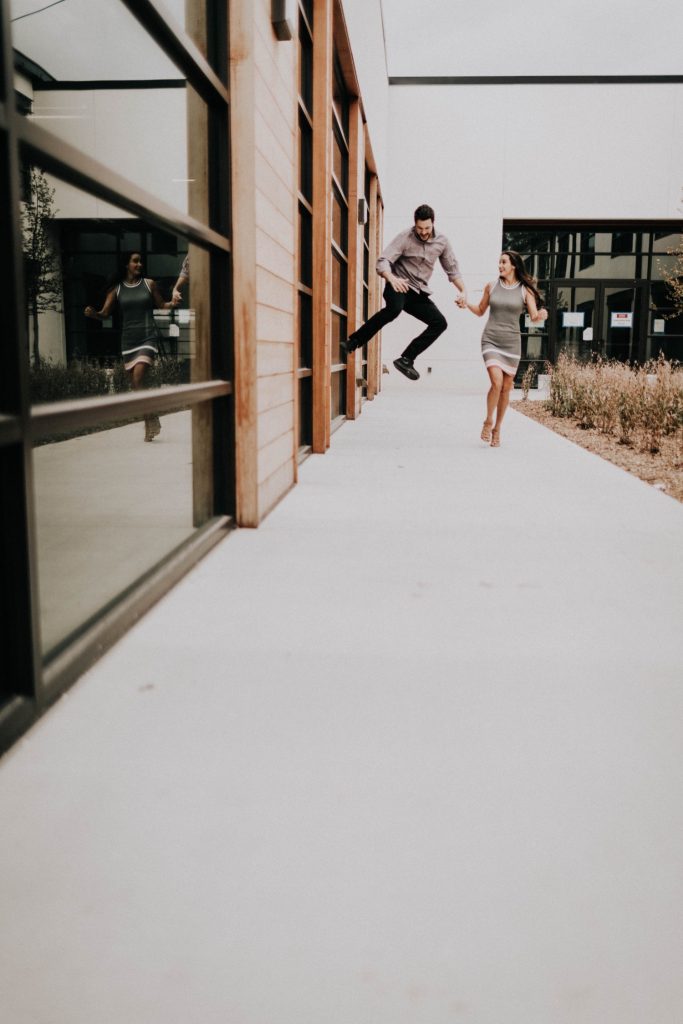 couple running with each other outside apartment during their at-home engagement