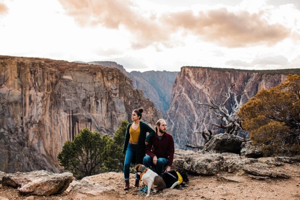 couple standing on the edge of a canyon cliff with their two dogs