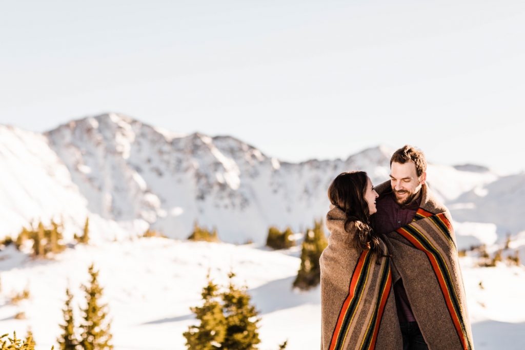 couple curled up in a Pendleton Yakima blanket during their snowy Colorado engagement photos in the Rocky Mountains