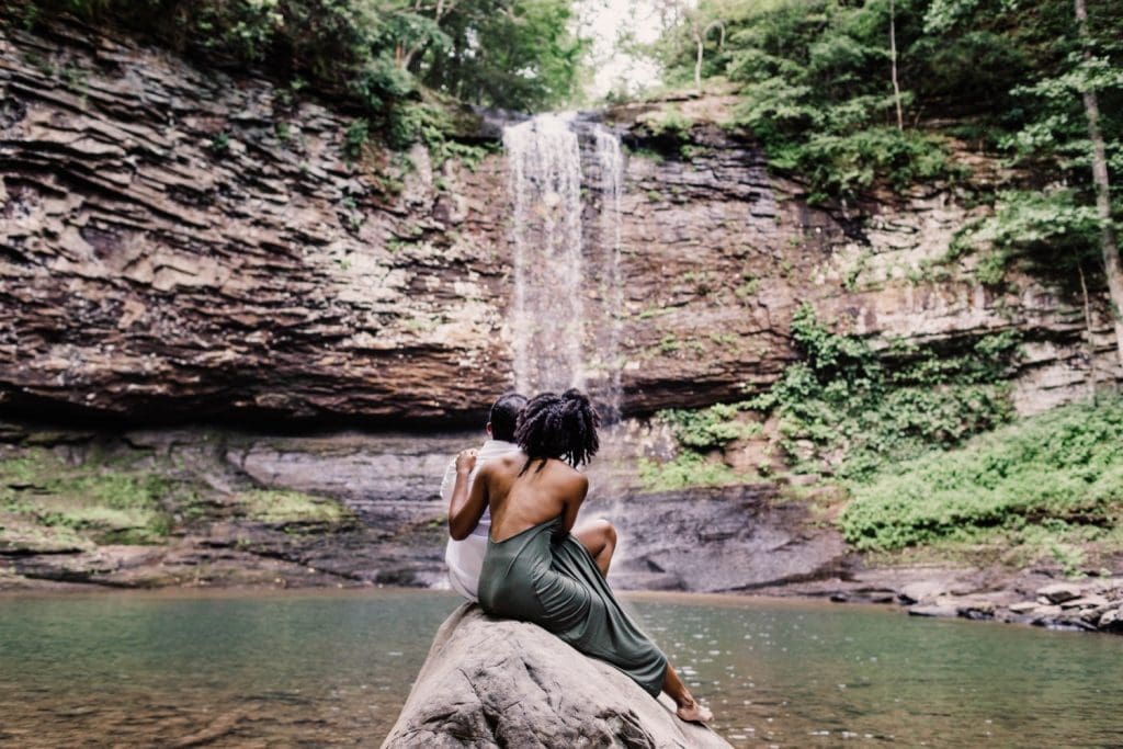 engaged couple sitting on a giant rock during their waterfall engagement photos
