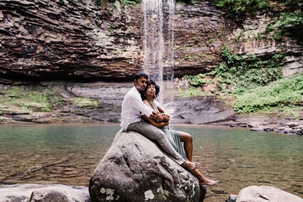 engaged couple sitting on a giant rock during their waterfall engagement photos