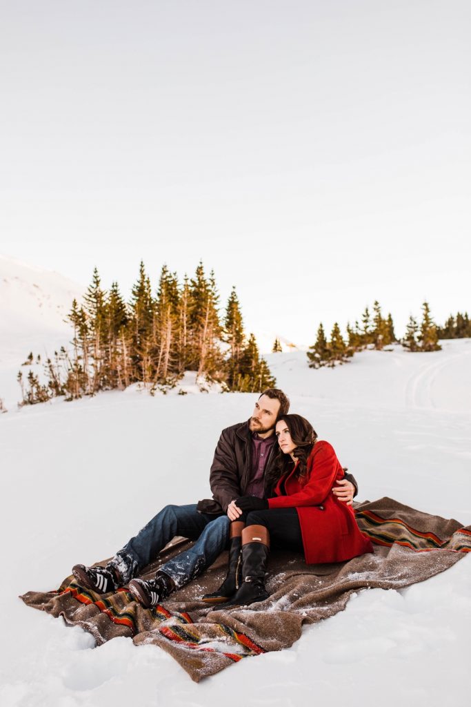 couple sitting on a Pendleton blanket during their snowy Colorado winter engagement photos in the Rocky Mountains
