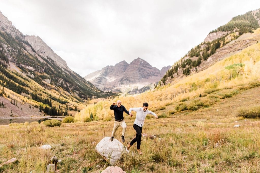 newly engaged same sex couple jumping off a rock in the mountains of Aspen Colorado after their Maroon Bells proposal