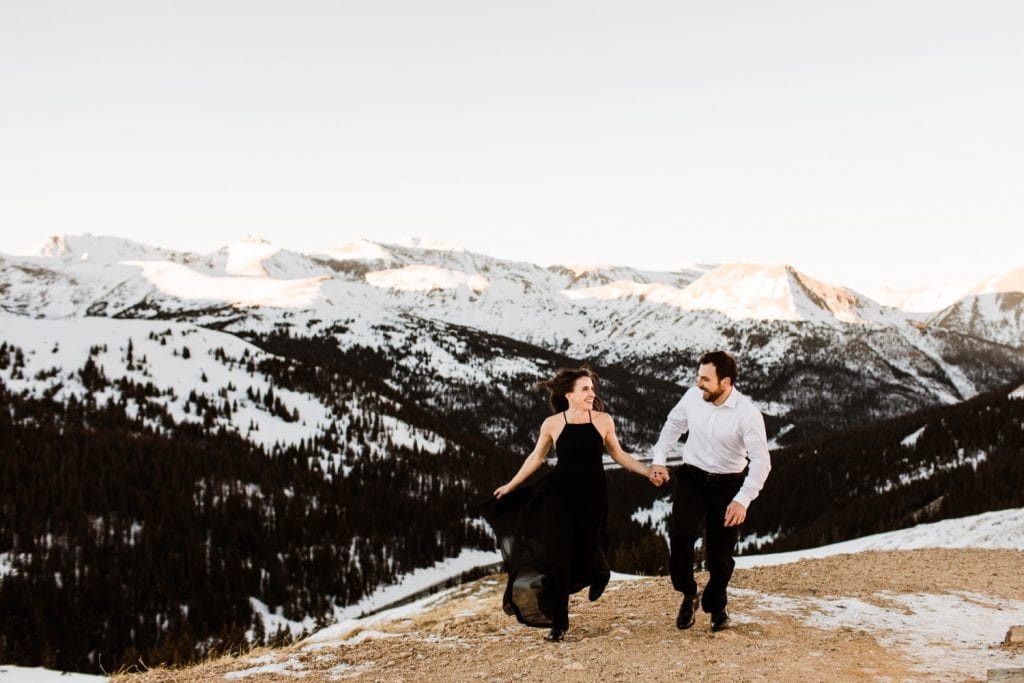 couple running through the snowy Rocky Mountains during their snowy Colorado engagement photos