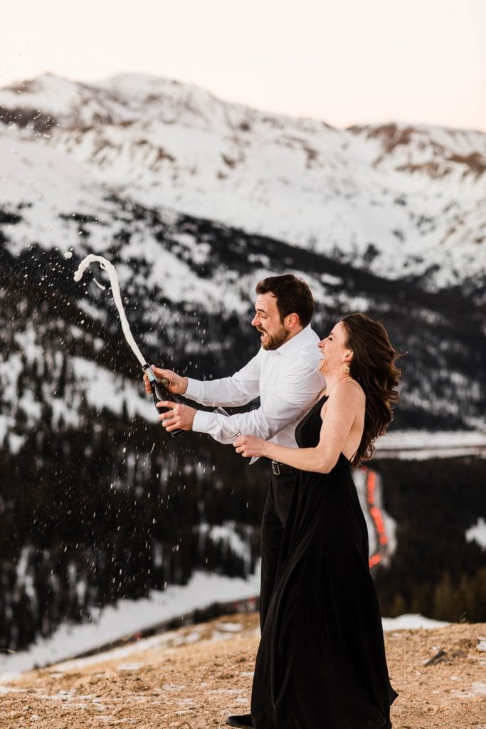 engaged couple popping champagne during their snowy Colorado winter engagement session