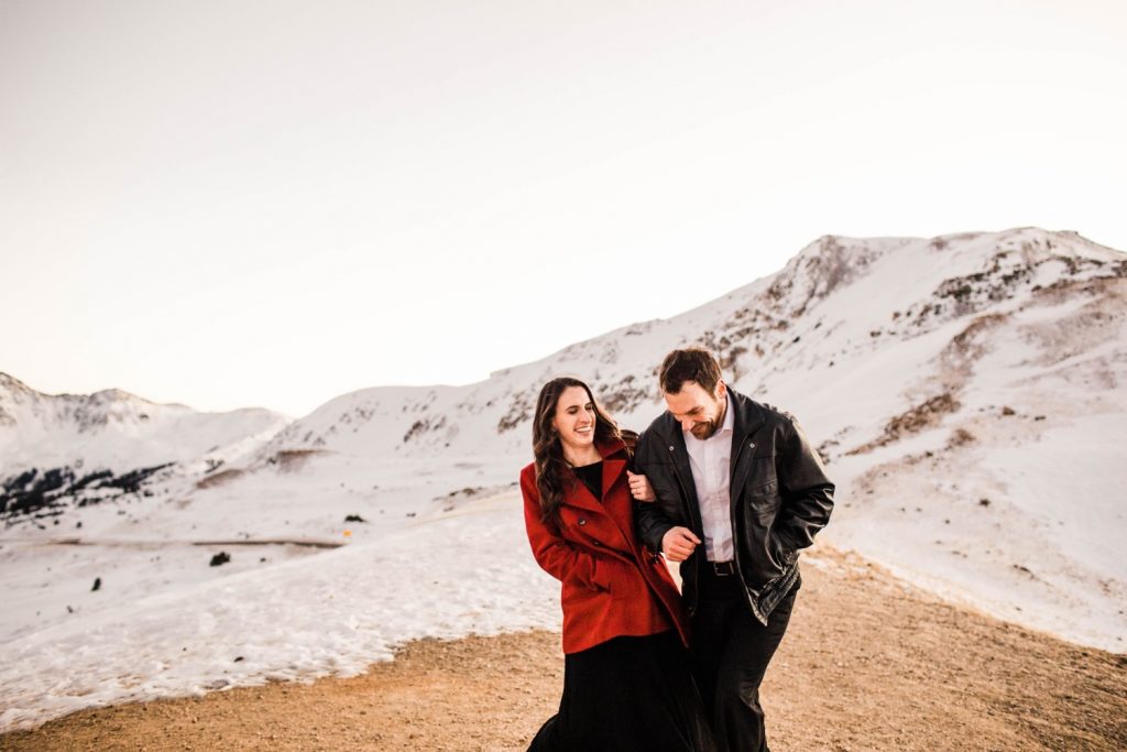 engaged couple laughing and running through the snowy mountains during their Colorado winter engagement photos in the Rockies