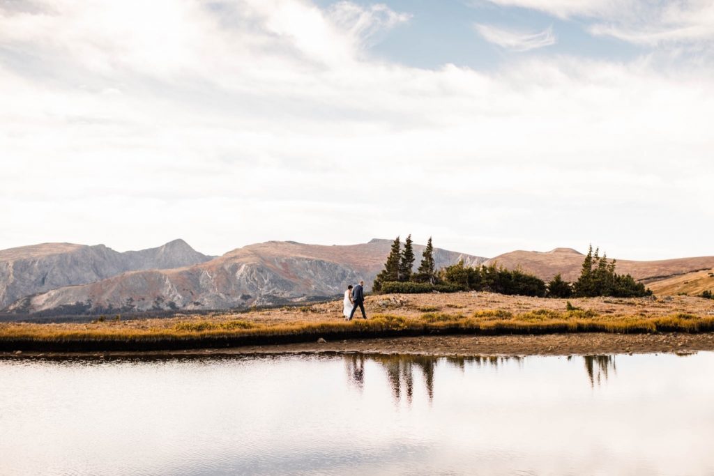 couple walking around a mountain lake during their Rocky Mountain post-wedding adventure session in Estes Park