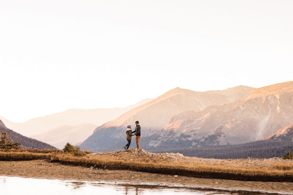 couple hiking around an alpine lake in the Rocky Mountains during their engagement session