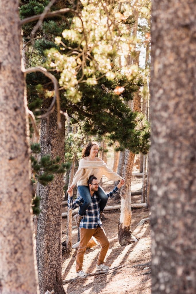 adventurous engaged couple running through the woods at sunrise during their Rocky Mountain National Park engagement photos in Colorado