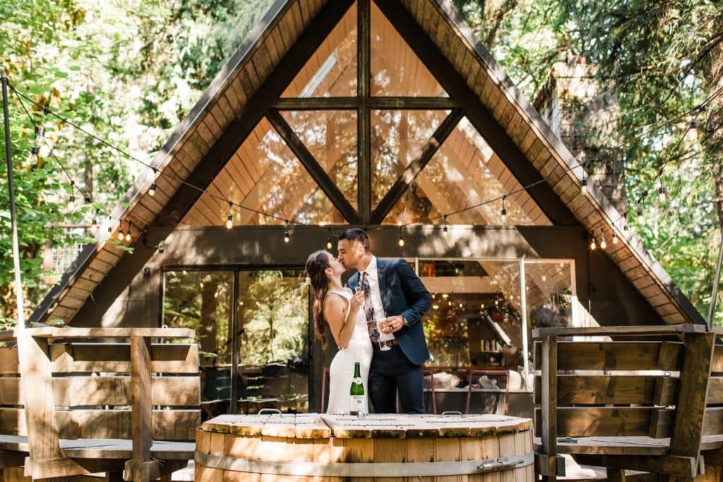 eloping couple popping champagne after their Mt Rainier elopement | Washington state elopement in an a-frame cabin