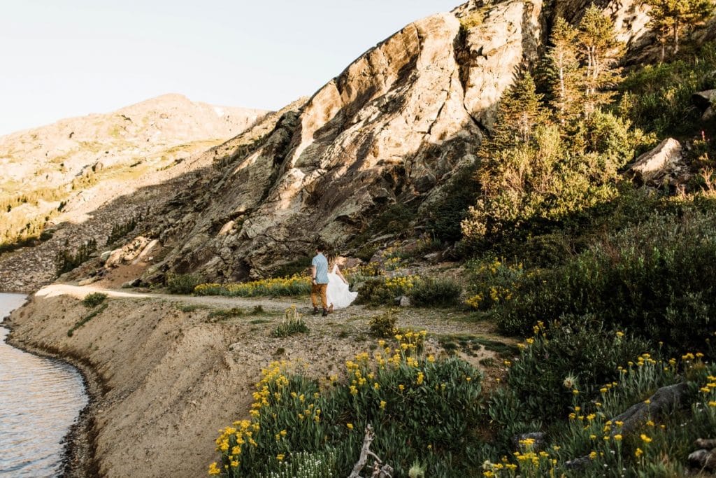 eloping couple running through a meadow of mountain wildflowers while holding hands | Breckenridge wedding photographers