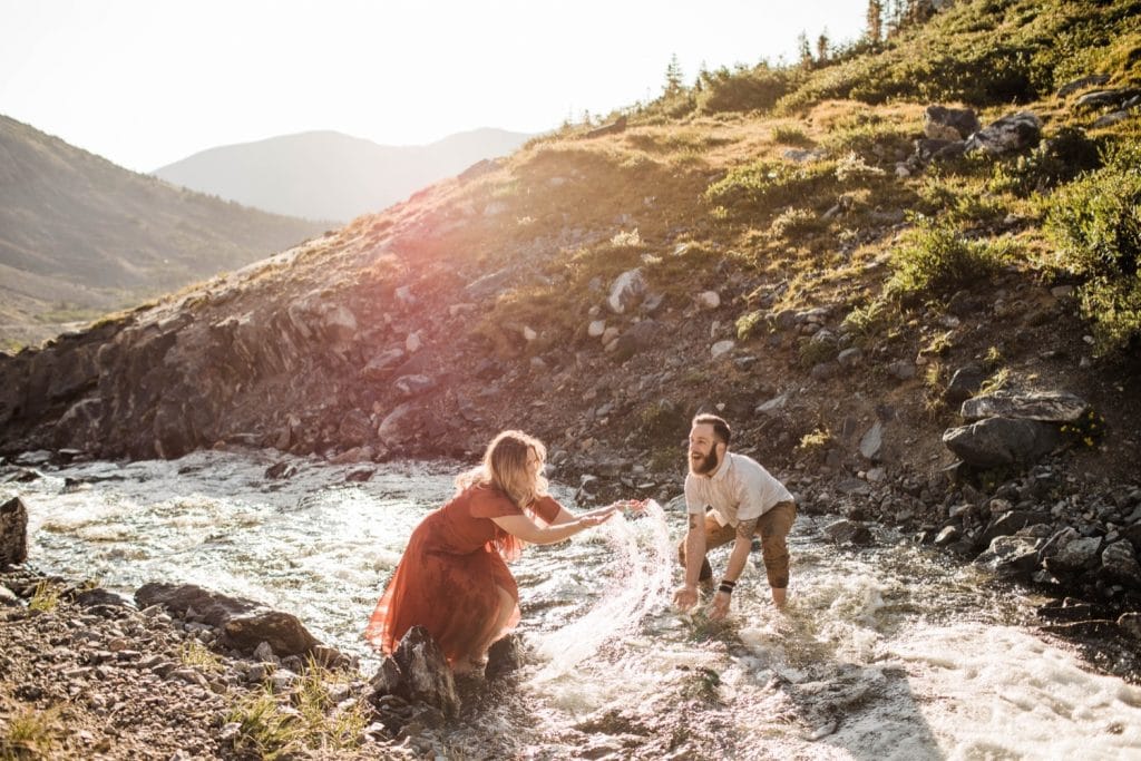 eloping couple splashing each other in a creek during their adventurous engagement photos in the mountains of Colorado | Breckenridge wedding photographers