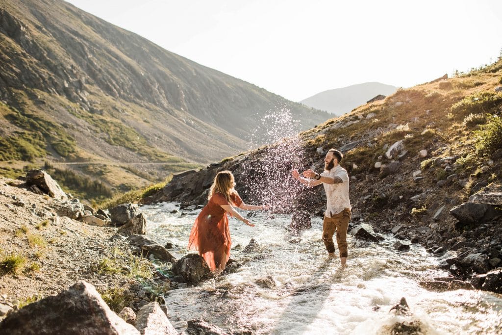 eloping couple splashing each other in a creek during their adventurous engagement photos in the mountains of Colorado | Breckenridge wedding photographers