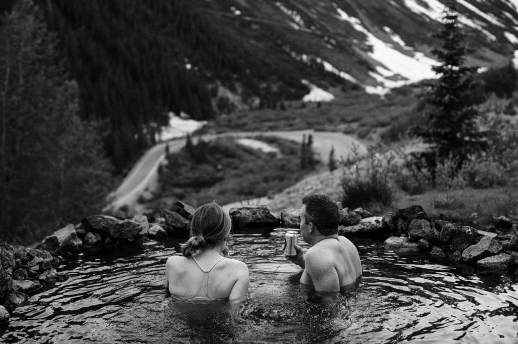 engaged couple drinking cider in a hot spring during their Telluride engagement photos in the San Juan mountains of southwest Colorado