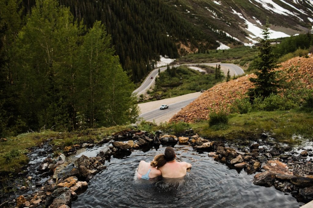 couple sitting together in a secret mountain hot spring in Telluride while getting their engagement photos taken