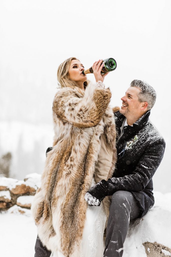 bride drinking champagne to celebrate her winter Sapphire Point elopement in the snow