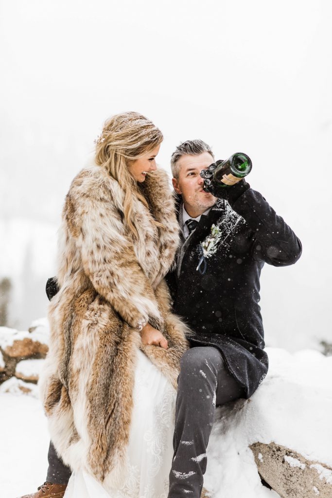 groom drinking champagne to celebrate his winter Sapphire Point elopement in the snow