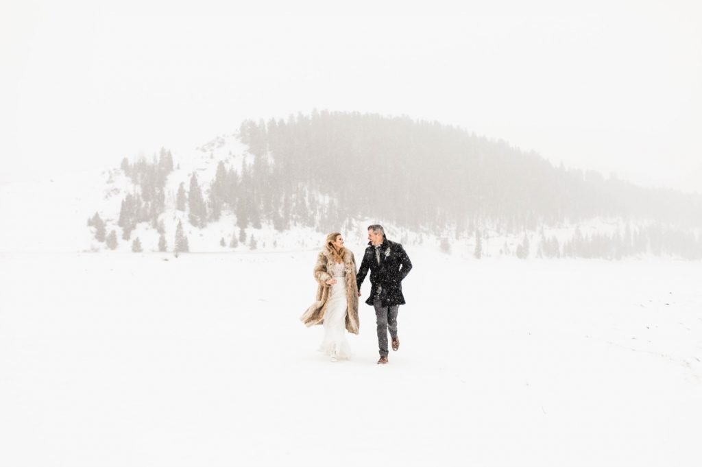 eloping couple running through the snow after their Sapphire Point elopement ceremony