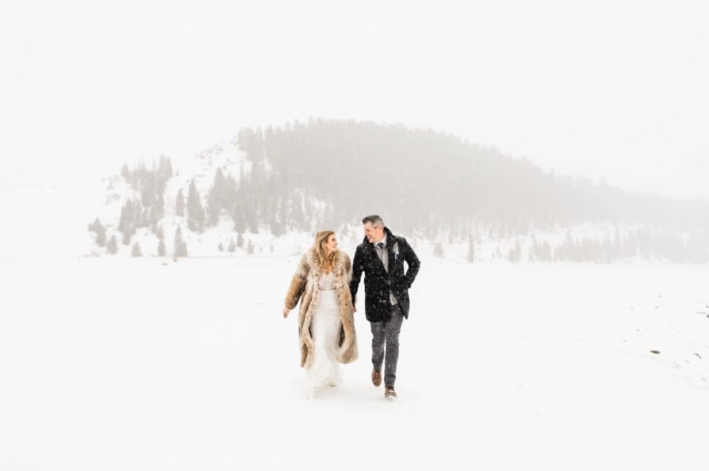 eloping couple running through the snow after their Sapphire Point elopement ceremony