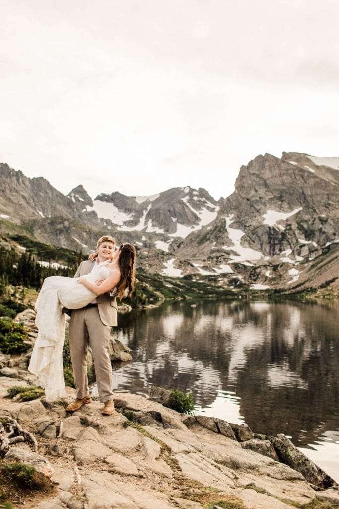 married couple hiking up a rock by an alpine lake during their mountain wedding in Colorado