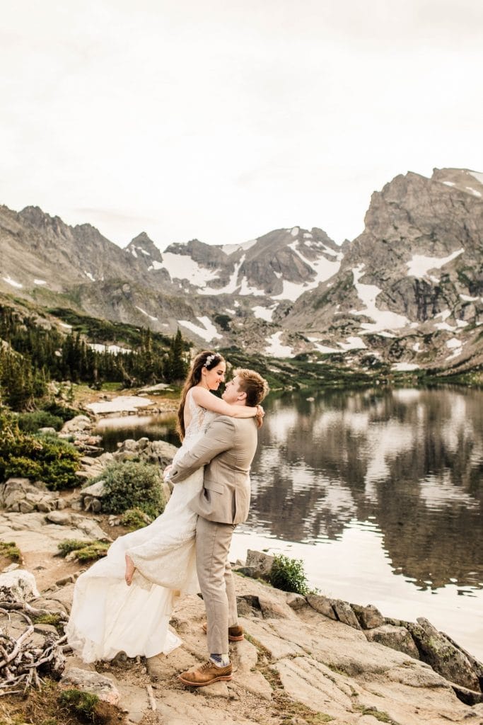 married couple hiking up a rock by an alpine lake during their mountain wedding in Colorado