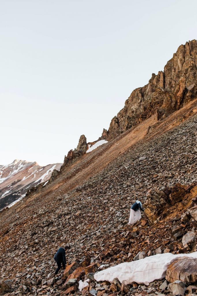 bride and groom scrambling up the side of a mountain to say their vows during their elopement in Telluride