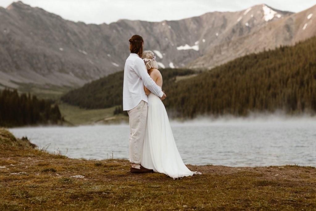 couple admiring a steaming alpine lake before they begin their lake wedding ceremony at sunrise