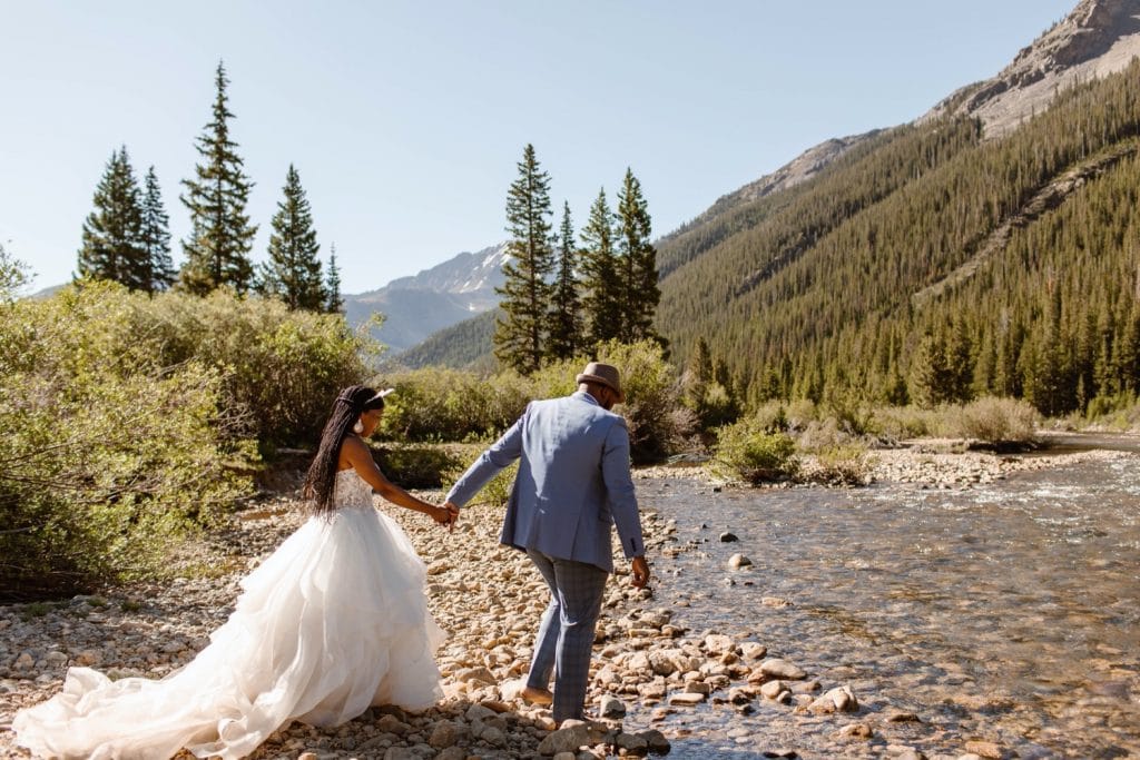 couple wading through a creek in their wedding attire after they eloped in Aspen Colorado