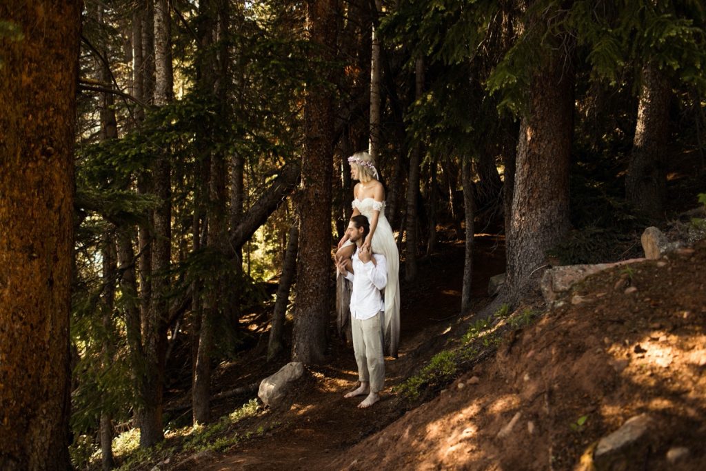 bride sitting on groom's shoulder while hiking in the forest after their elopement ceremony