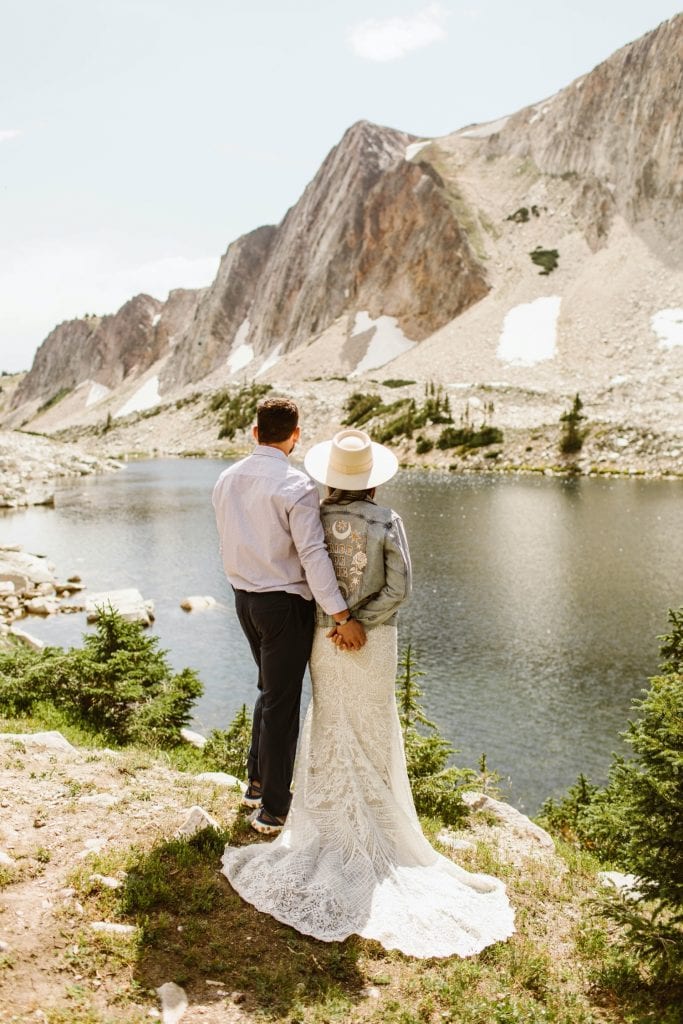 bride and groom standing next to each other and looking out onto a lake in the Snowy Range Mountains after their Wyoming elopement - bride wearing Rue de Seine denim