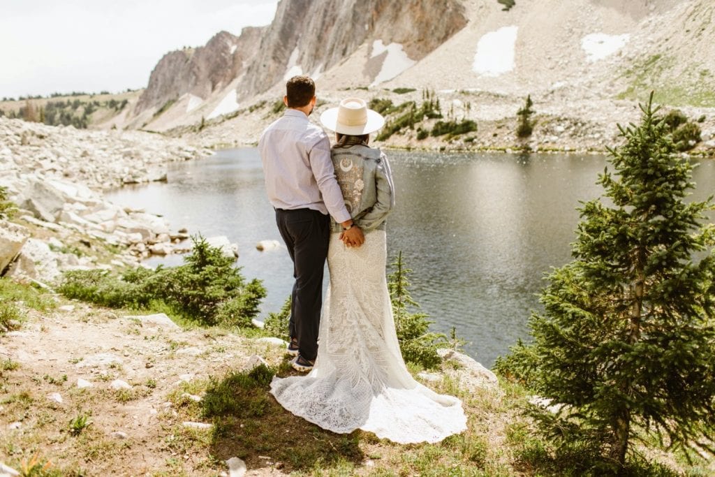 bride and groom standing next to each other and looking out onto a lake in the Snowy Range Mountains after their Wyoming elopement - bride wearing Rue de Seine denim
