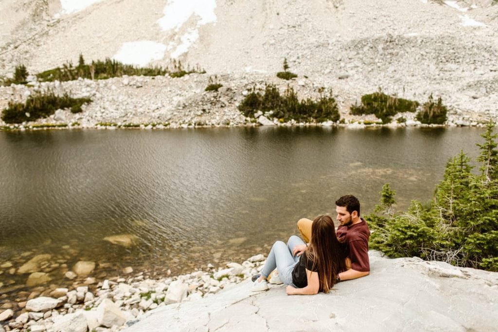 couple sunbathing on a rock together by the lake while having their mountain engagement photos taken