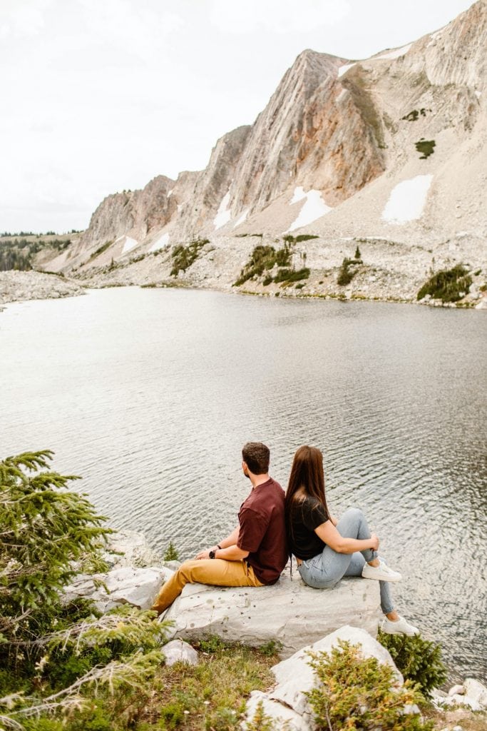 mountain engagement photos of a couple sitting by an alpine lake in Wyoming