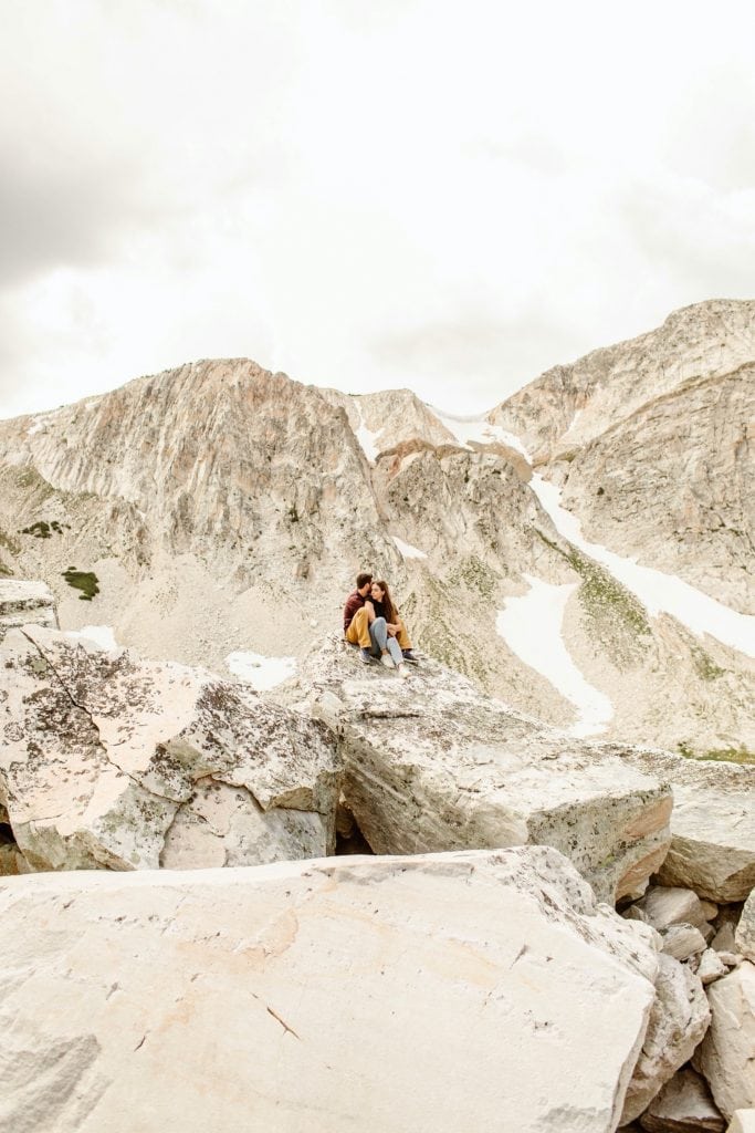 engaged couple sitting on a rocky mountain top during their mountain engagement photos in Wyoming