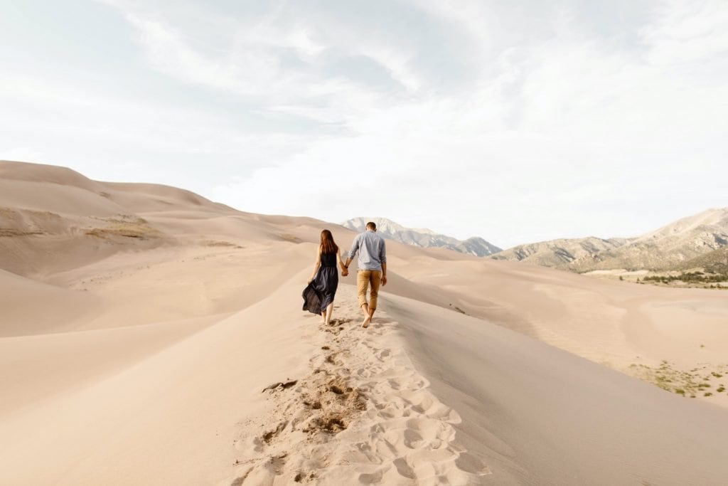 sand dunes engagement photos of a couple walking on the dune ridge