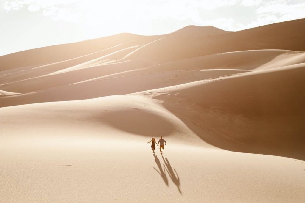 couple running down the giant dune field during their sand dunes engagement photos