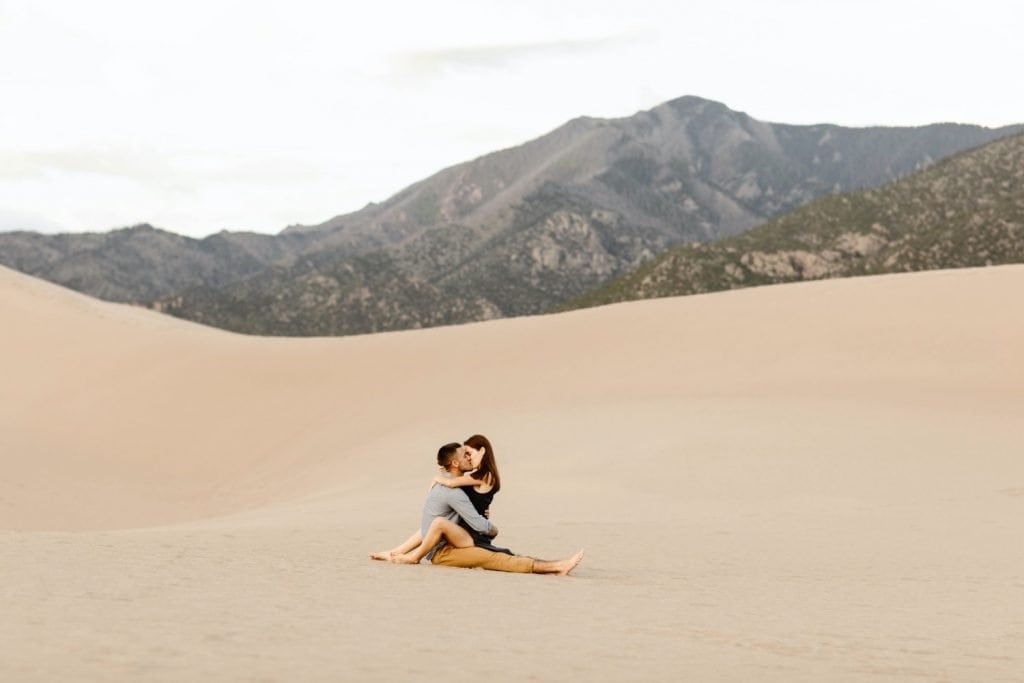 sand dunes engagement photos of couple kissing while sitting on the sand