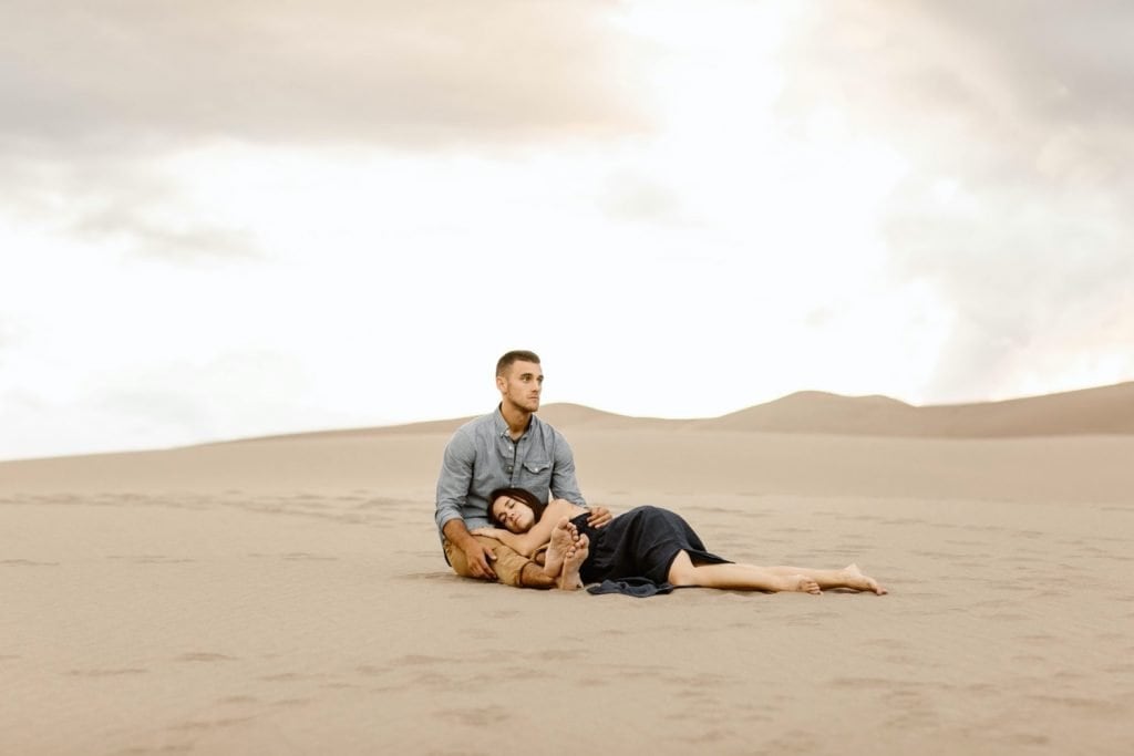 couple sitting on the ground during their sand dunes engagement photos
