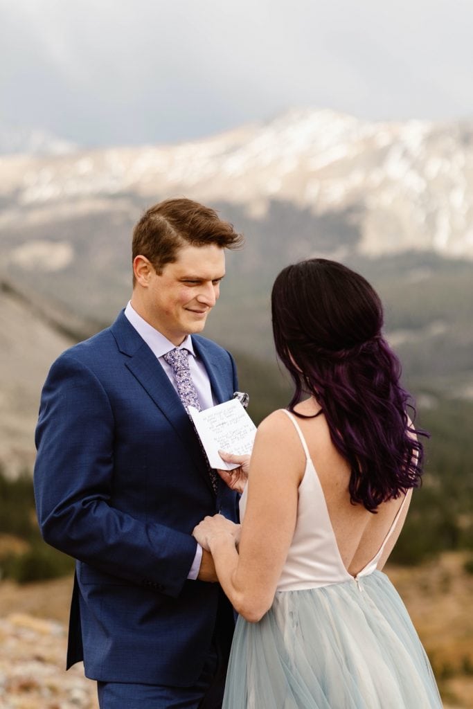 groom smiling at bride while she reads her vows