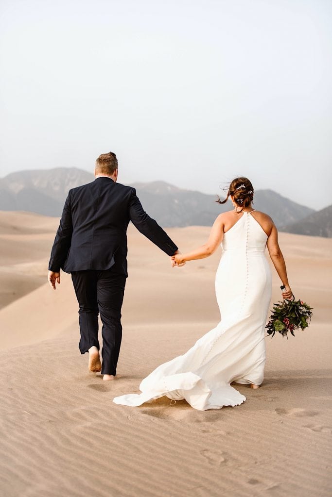 bride and groom trekking across the dune field after their Great Sand Dunes National Park elopement ceremony