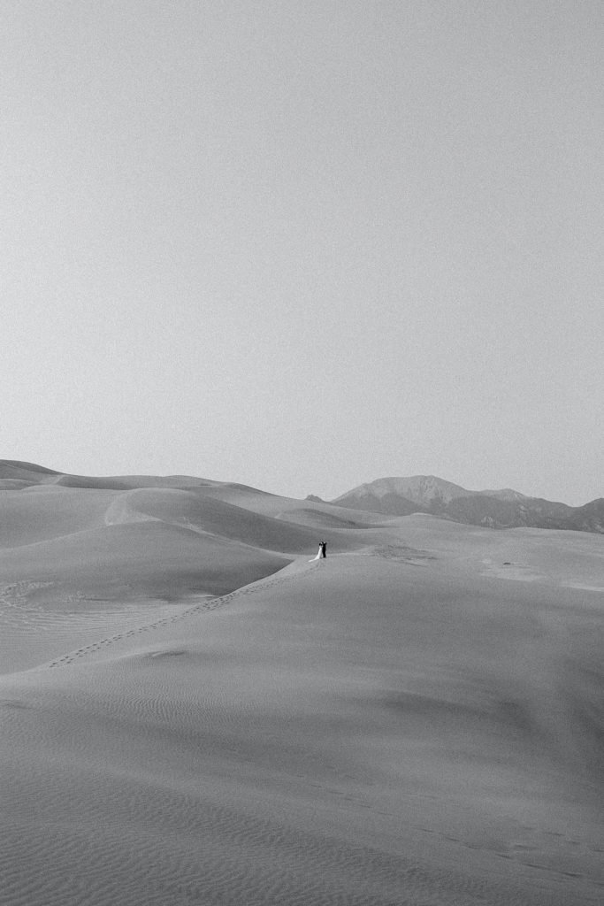 bride and groom trekking across the dune field after their Great Sand Dunes National Park elopement ceremony