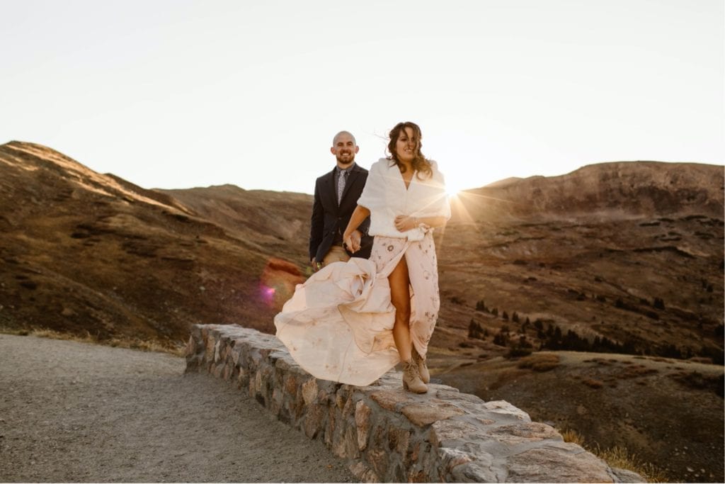 eloping couple walking on a stone wall in the mountains at sunset after their Colorado micro wedding ceremony