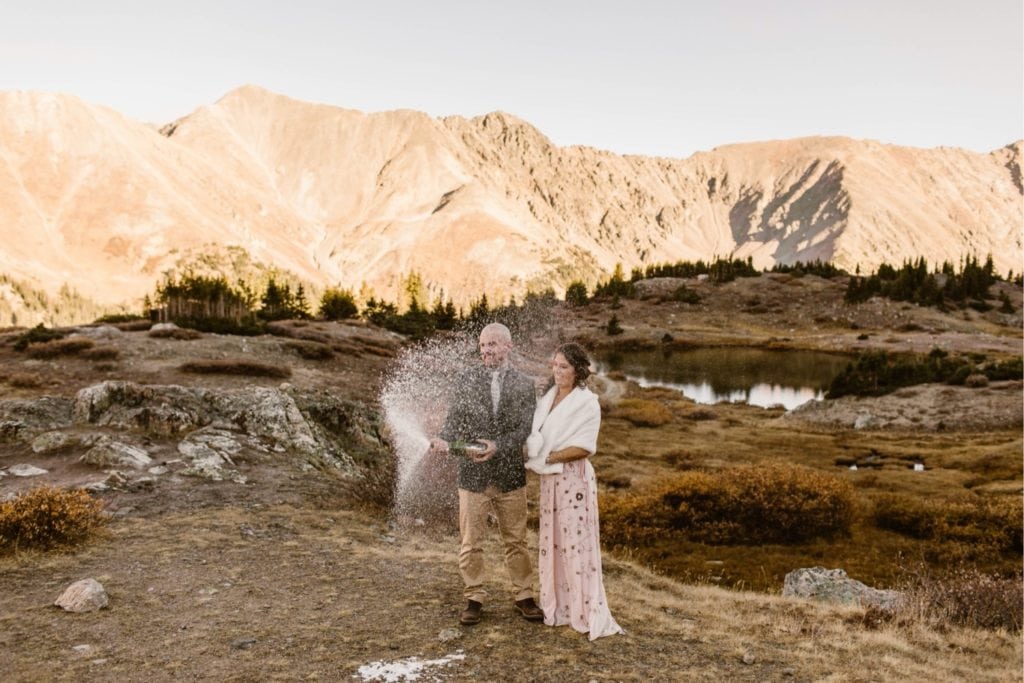 couple popping champagne at their Colorado micro wedding in the mountains near Denver