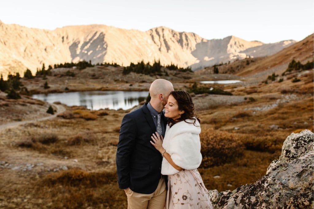 groom whispering funny jokes into bride's ear while they stand together to stay warm in the mountains of Colorado