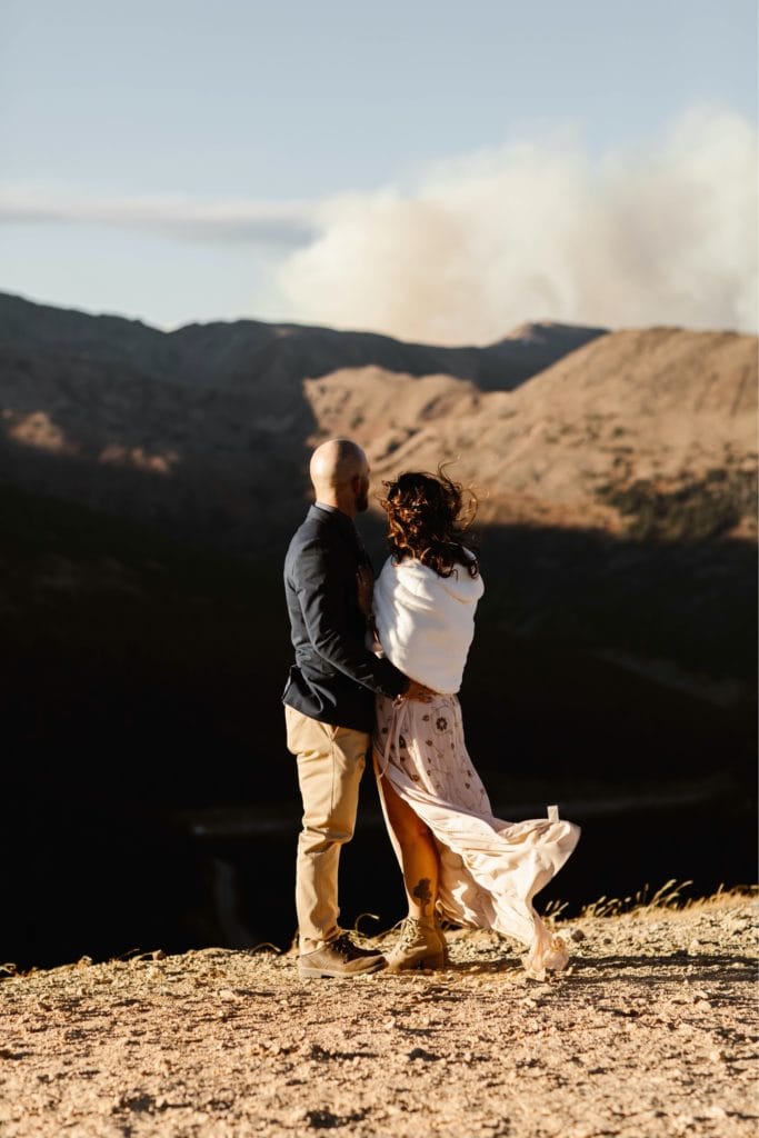 couple standing together on an overlook in the mountains while looking out a plume of wildfire smoke in Colorado