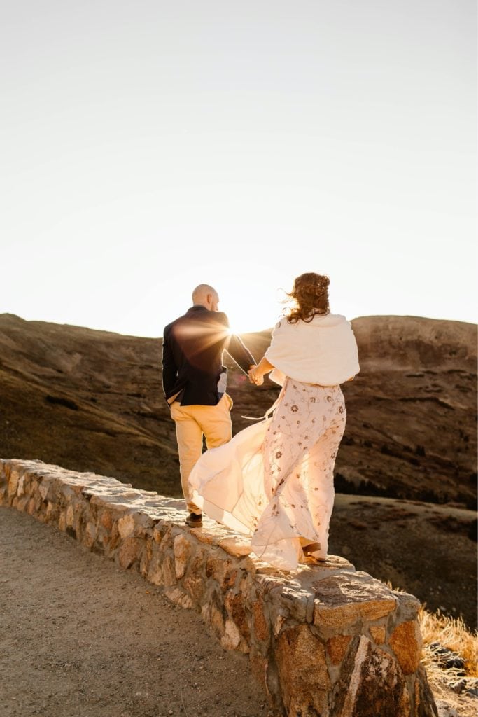 eloping couple walking on a stone wall in the mountains at sunset after their Colorado micro wedding ceremony