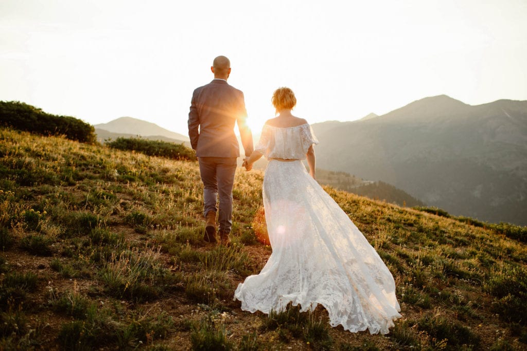 eloping couple walking in the mountains while the bride wears a two piece summer elopement dress