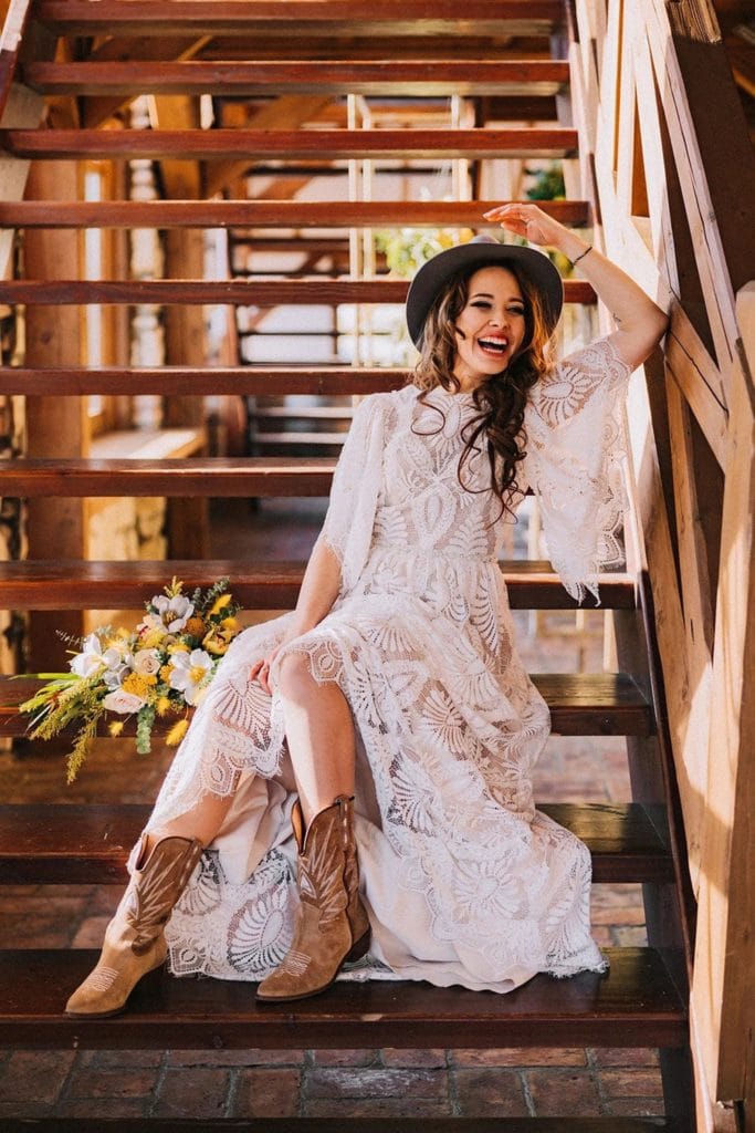 bride wearing a bohemian high neck fringe and lace summer elopement dress and wearing a hat and cowboy boots