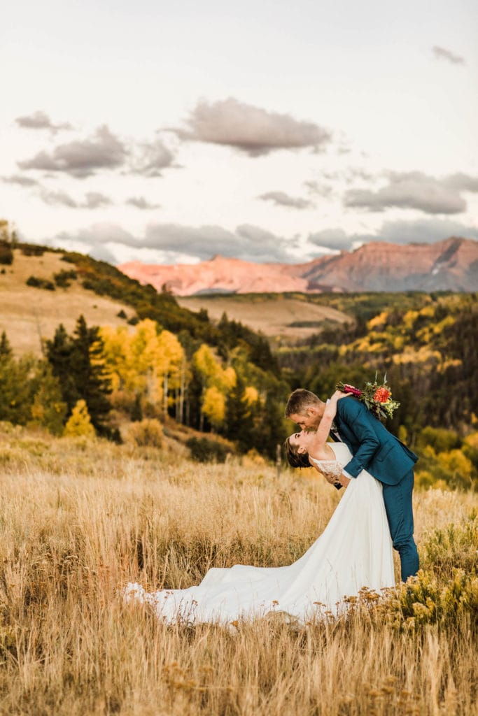 couple kissing in a mountain meadow while the bride wears a flowy elopement dress for fall with a dramatic train